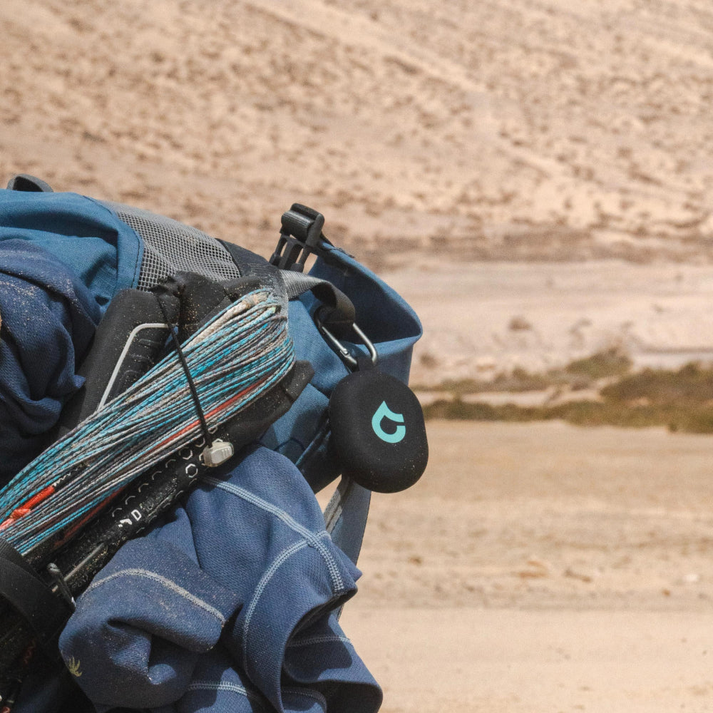 Backpack loaded with outdoor and water-sports gear resting on sandy ground.